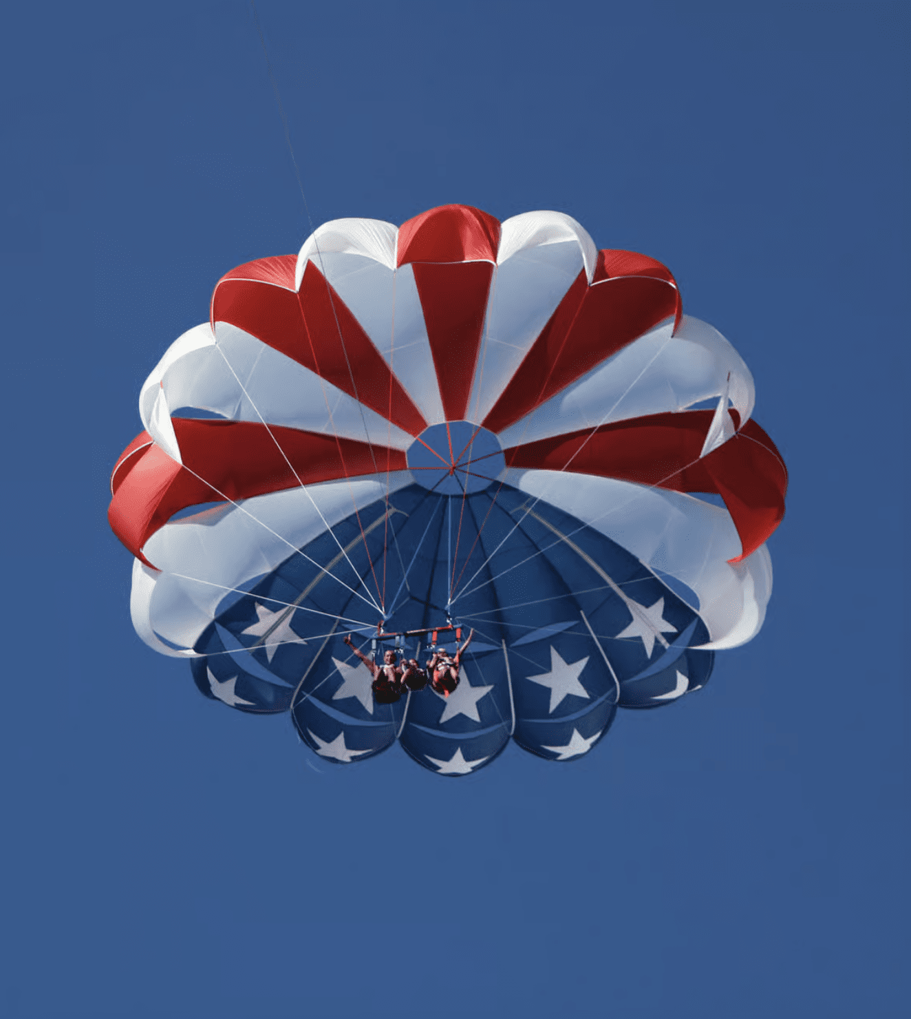 Parasailers flying beneath a patriotic red, white, and blue parachute over Clearwater Beach.