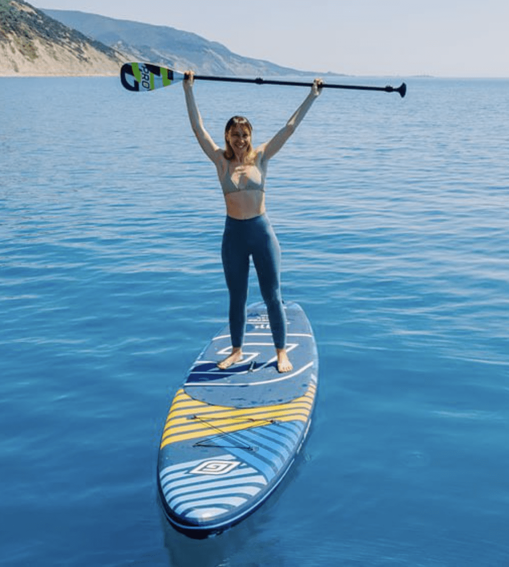 Woman standing on a paddleboard raising a paddle over crystal-clear blue water.