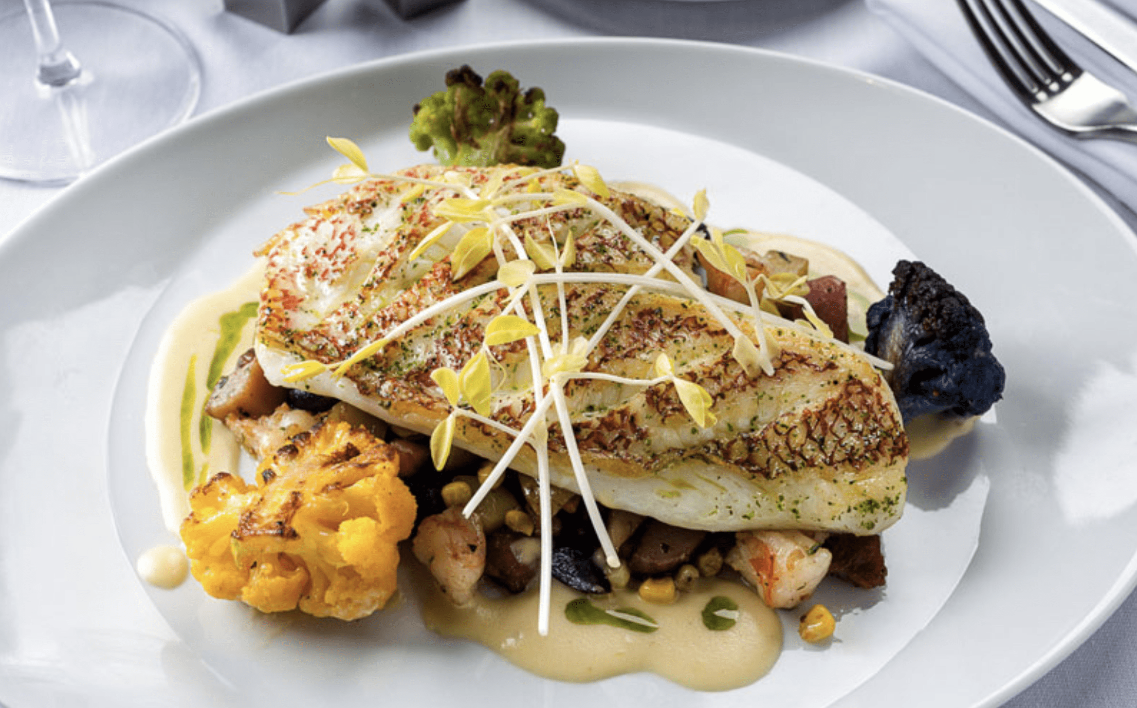 Gourmet fish fillet served with roasted vegetables, cauliflower, and creamy sauce