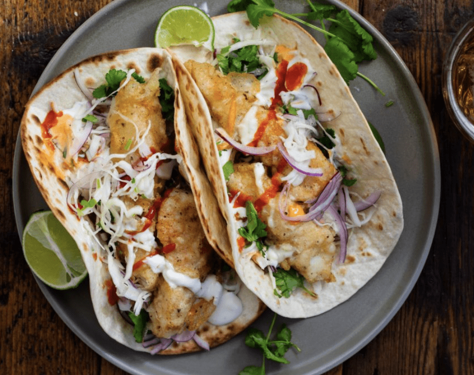 Fish tacos with crispy batter, shredded cabbage, red onion, cilantro, and fresh lime slices