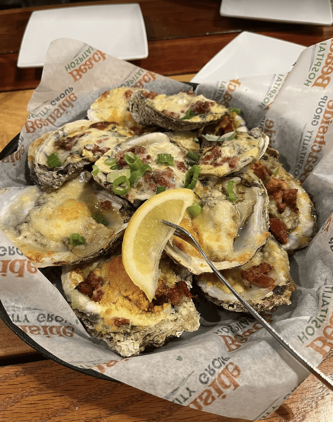 Baked oysters topped with cheese, bacon, and green onions, served with a lemon wedge.