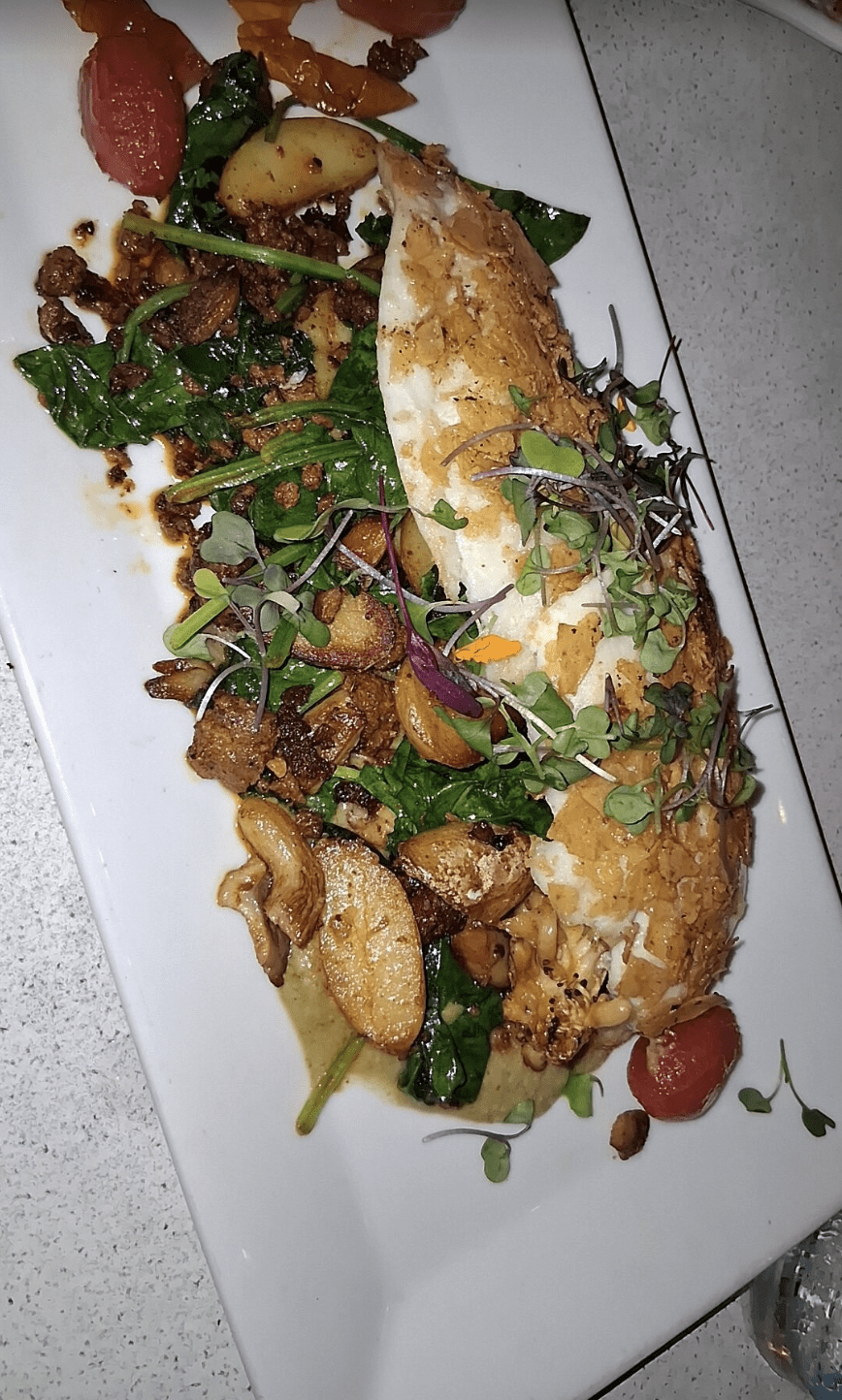 Pan-seared fish fillet served with sautéed potatoes, spinach, peppers, and fresh microgreens.