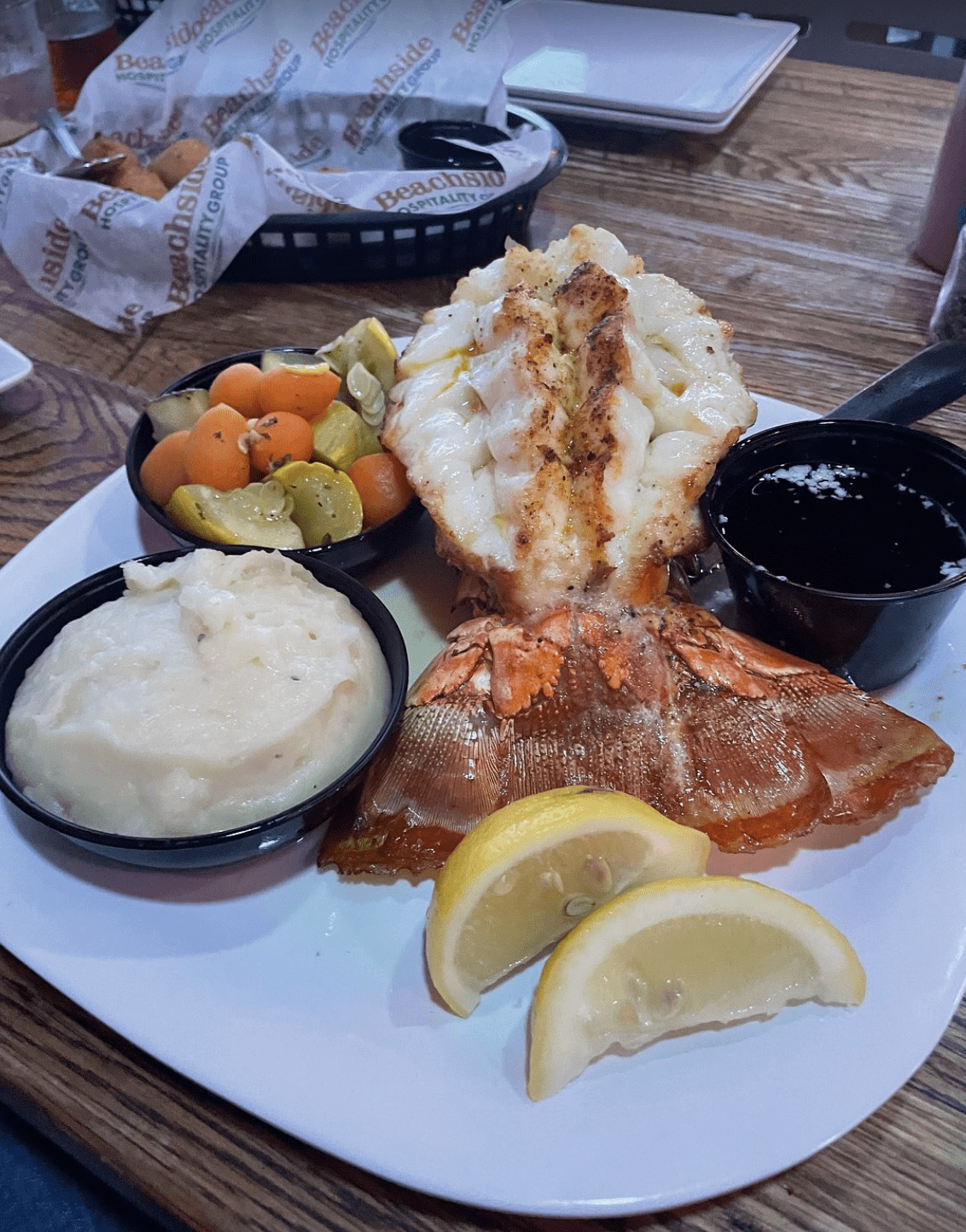 A broiled lobster tail served with mashed potatoes, sautéed vegetables, lemon wedges, and melted butter.