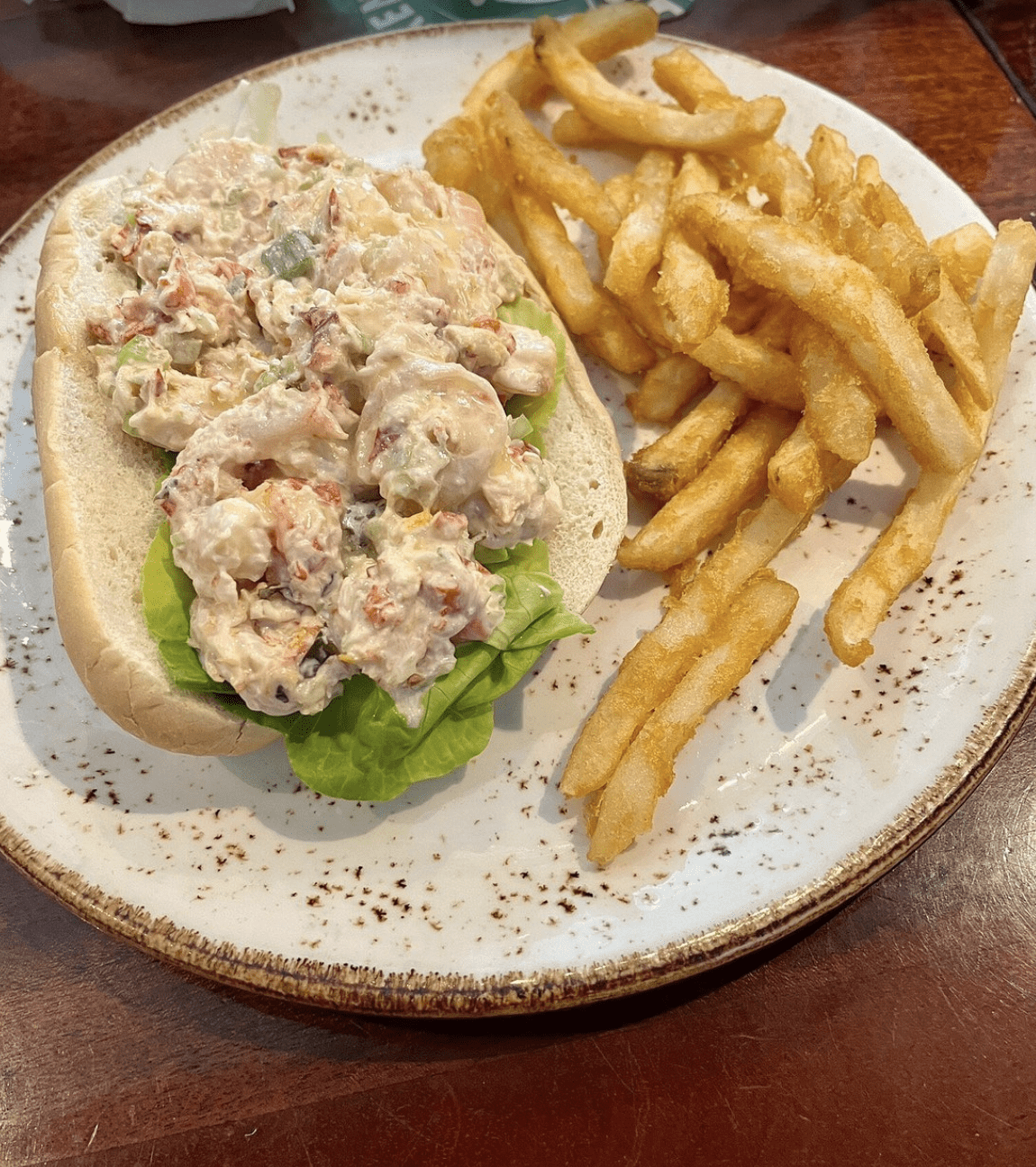 A shrimp salad roll in a soft bun with lettuce, served alongside golden French fries.