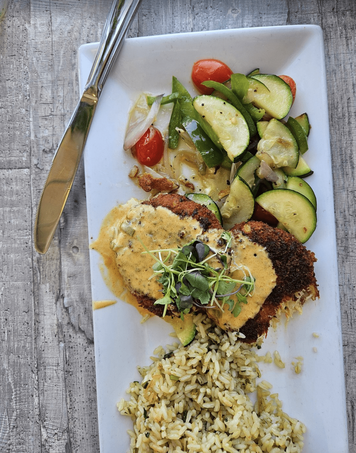 Crispy breaded fish fillets topped with a creamy sauce, served with sautéed zucchini, peppers, onions, and cherry tomatoes.