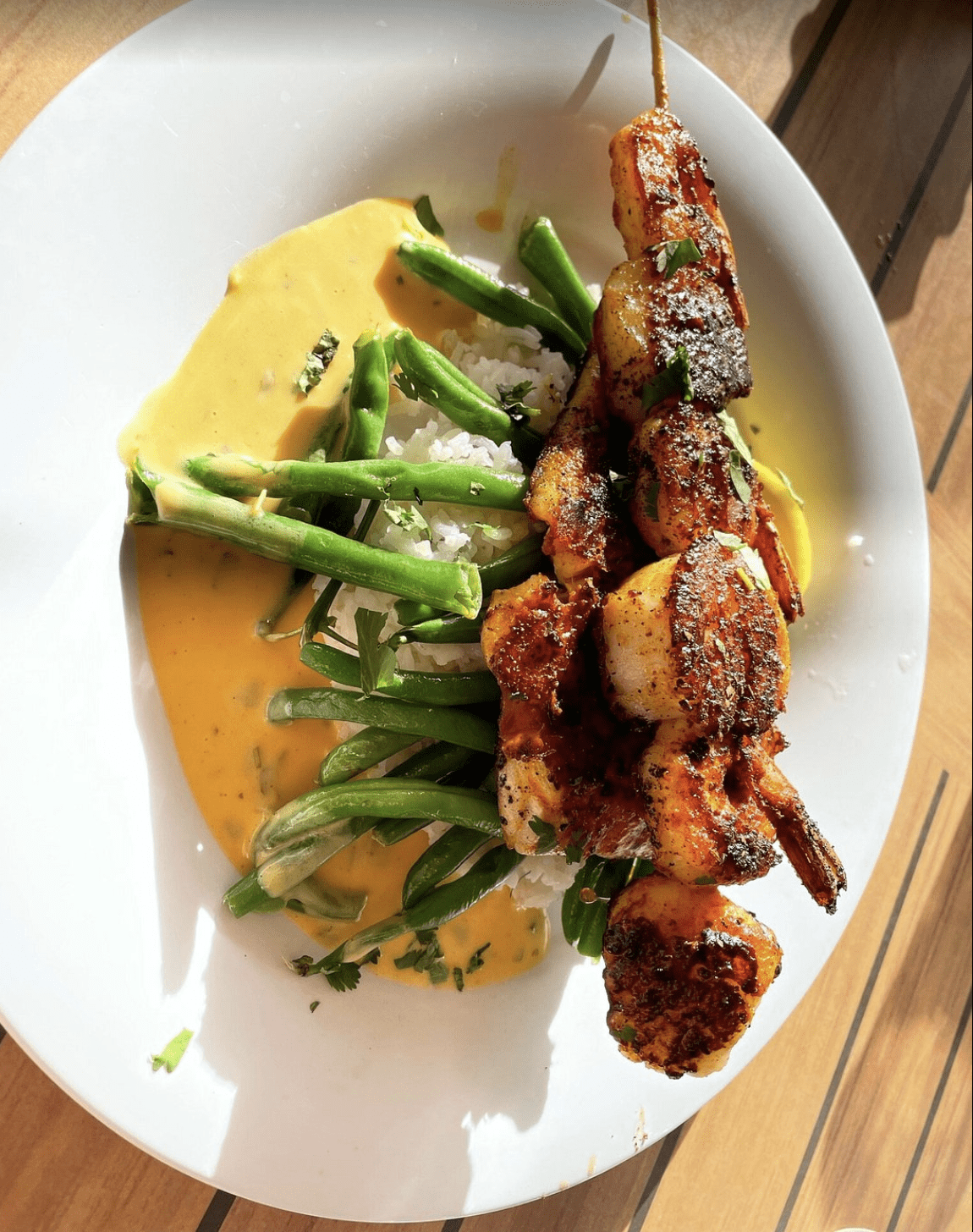 Grilled shrimp skewers served with white rice, green beans, and curry sauce.